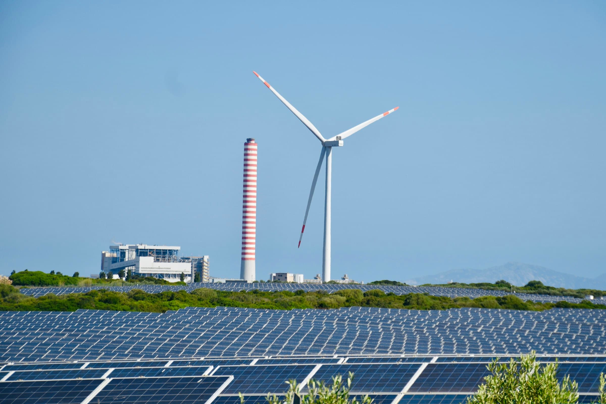 Solar panel field and wind turbine under a clear blue sky